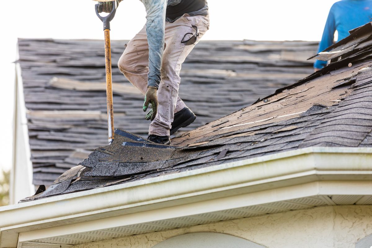 A man using a shovel to work on a roof, focused on his task under clear blue skies.