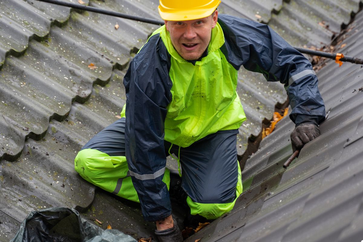 A man in bright yellow safety gear is positioned on a rooftop, focused on his work or inspection tasks.